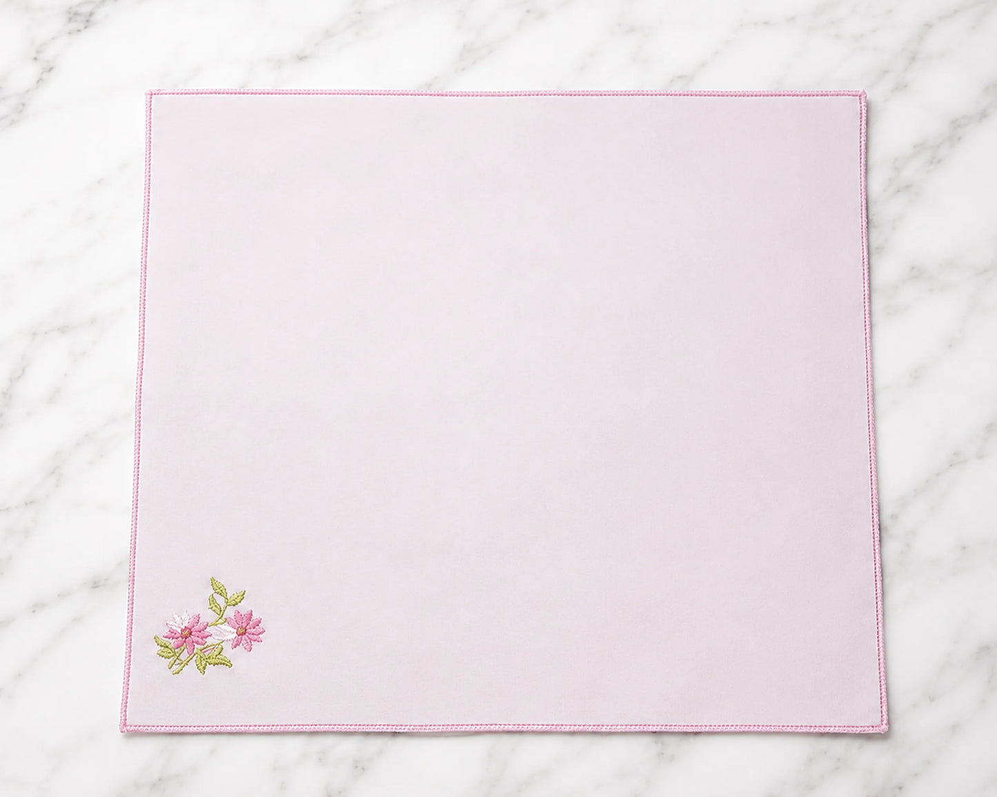 Pink placemat with floral embroidery on a marble surface