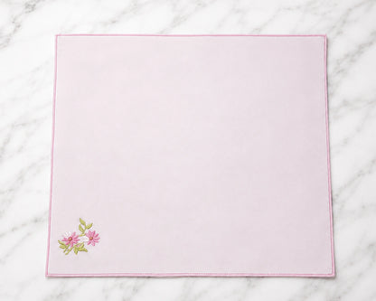 Pink placemat with floral embroidery on a marble surface