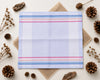 Plaid fabric with colorful stripes on a light background with decorative elements like pine cones and twigs.