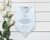 Light blue handkerchief with lace trim and personalized text on a wooden surface with flowers.