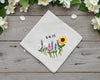 Natural linen colored handkerchief showcasing a detailed sunflower and wildflower garden embroidery with custom date text