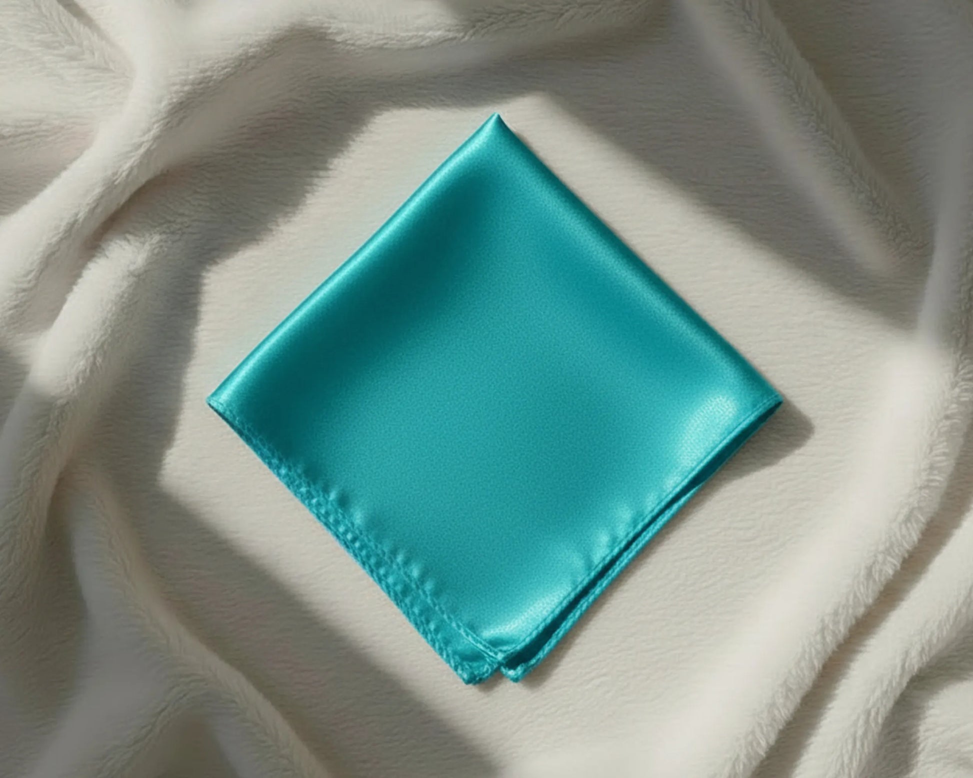 Turquoise satin square on a textured beige surface