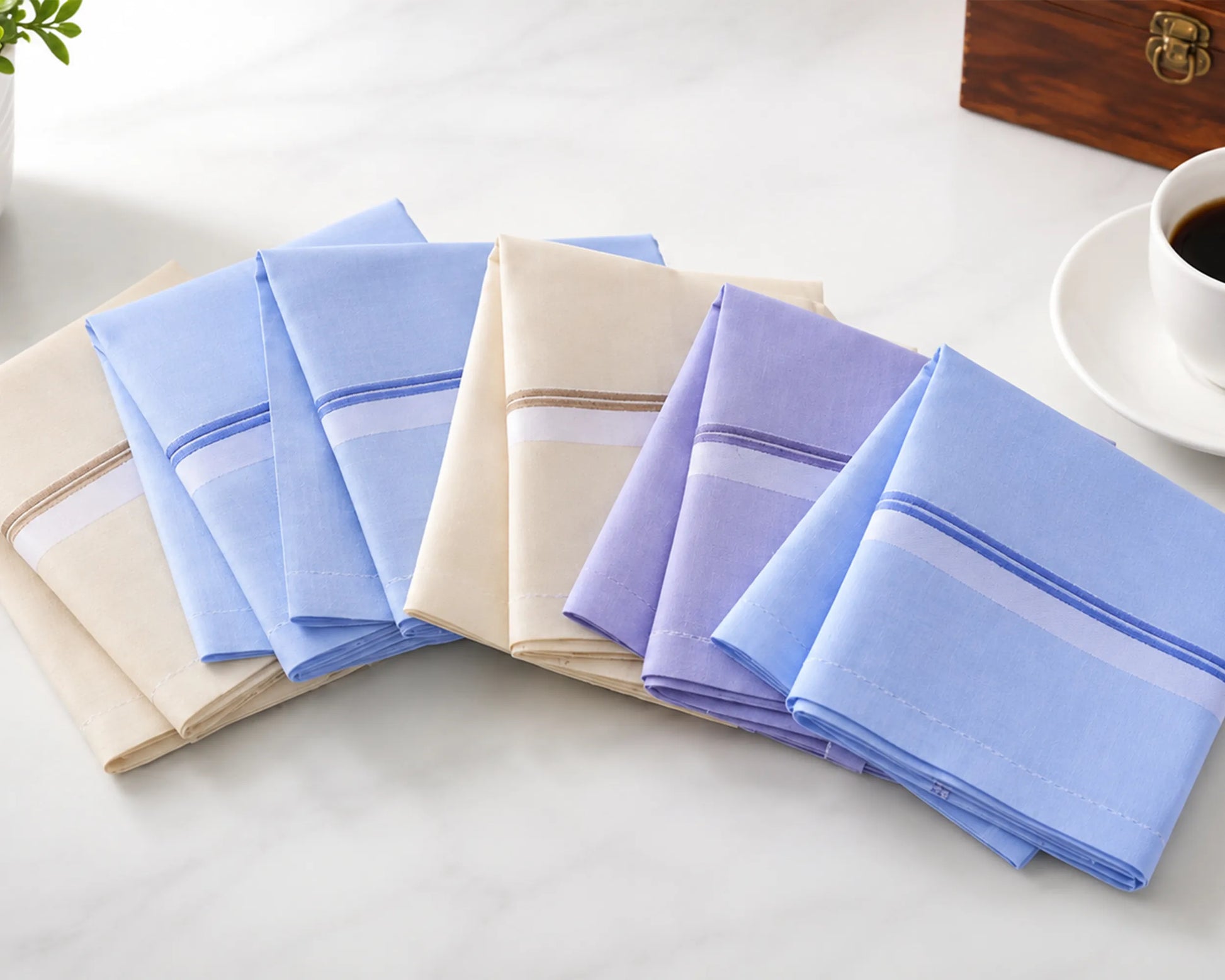 Set of folded handkerchiefs in various colors on a light surface with a cup of coffee in the background.