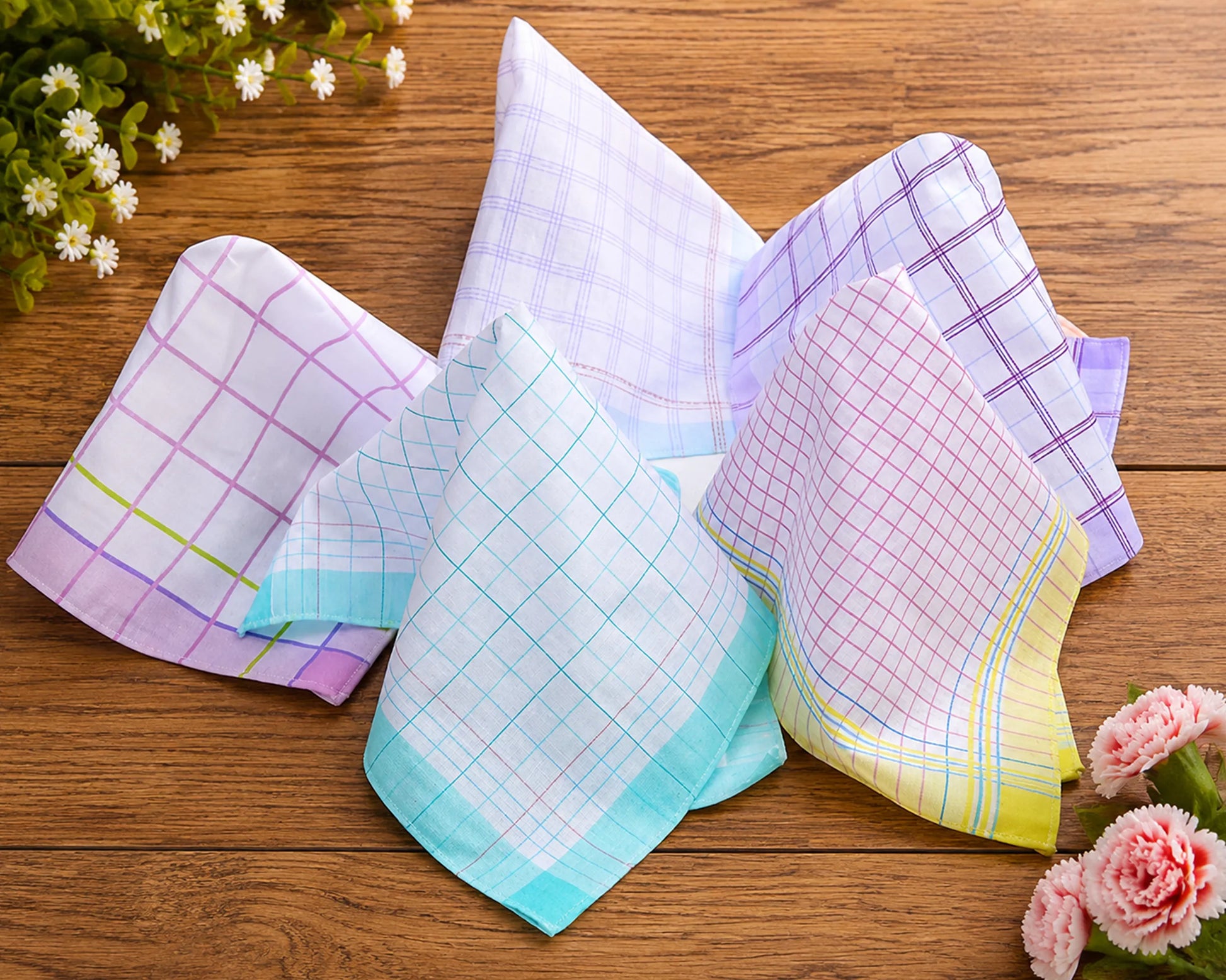 Set of colorful checkered handkerchiefs on a wooden surface with flowers.