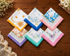 Set of colorful floral handkerchiefs on a wooden surface with flowers and lace.