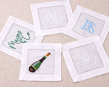 Set of embroidered cocktail napkins with various designs on a beige surface