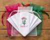Set of embroidered handkerchiefs with floral design and text, surrounded by colorful drawstring bags on a wooden surface.