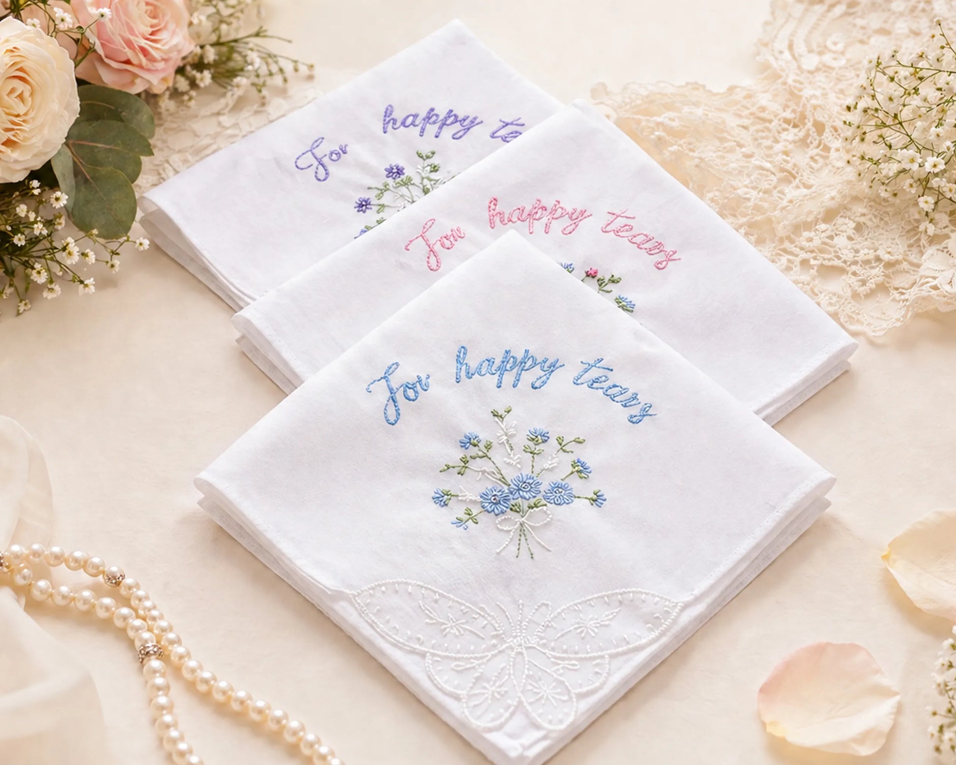 Set of embroidered handkerchiefs with floral designs and text on a decorative surface with flowers and pearls.