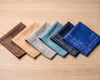 Set of five patterned hanky in brown, beige, gray, blue, and navy on a wooden surface.