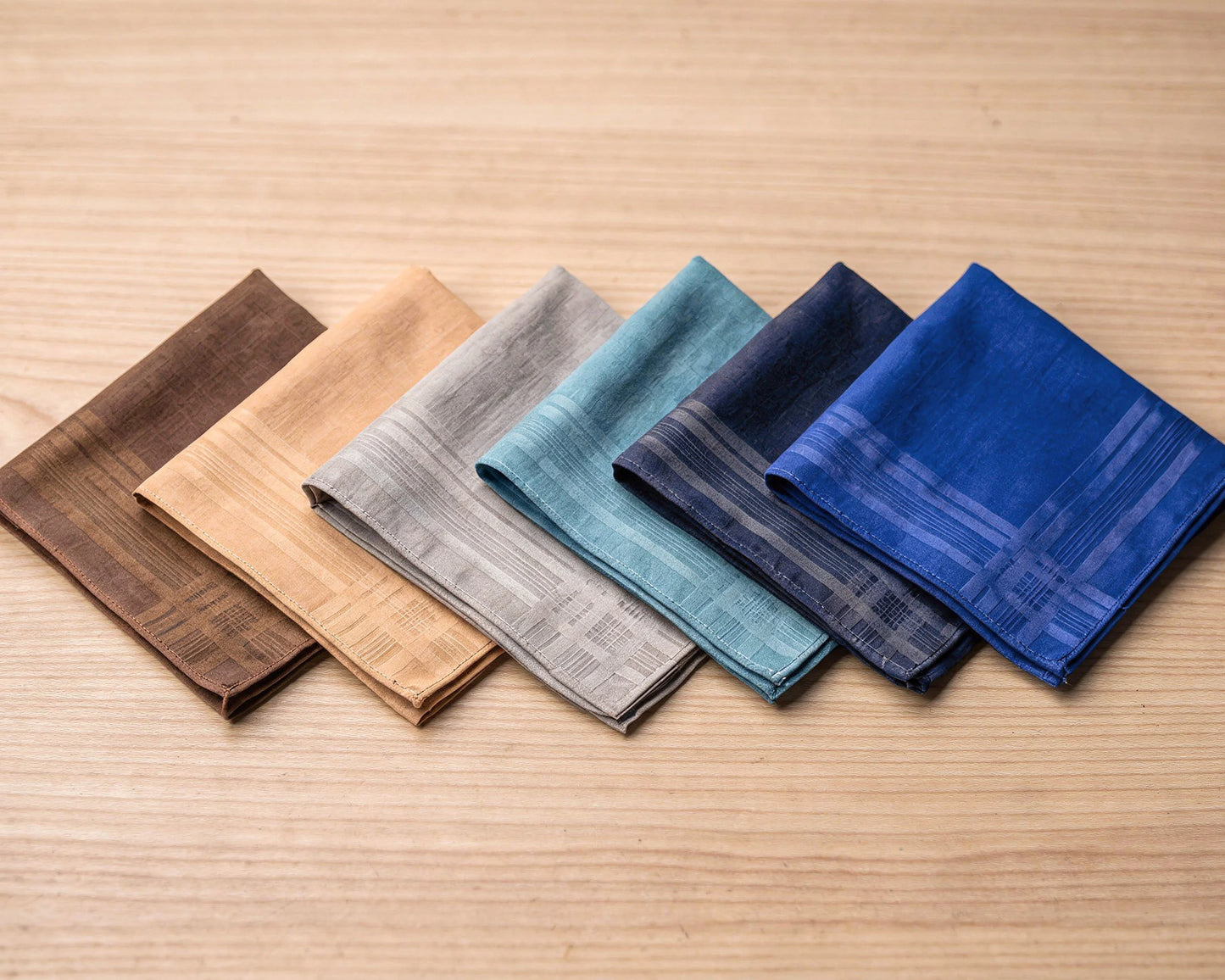 Set of five patterned hanky in brown, beige, gray, blue, and navy on a wooden surface.