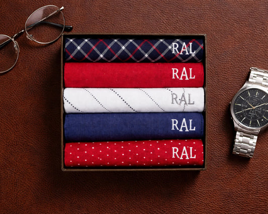 Set of folded HANKY with 'RAL' branding on a brown surface, next to eyeglasses and a watch.
