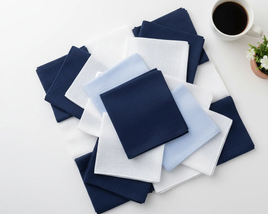 Set of folded blue, white, and gray hanky on a light surface with a coffee cup and plant.