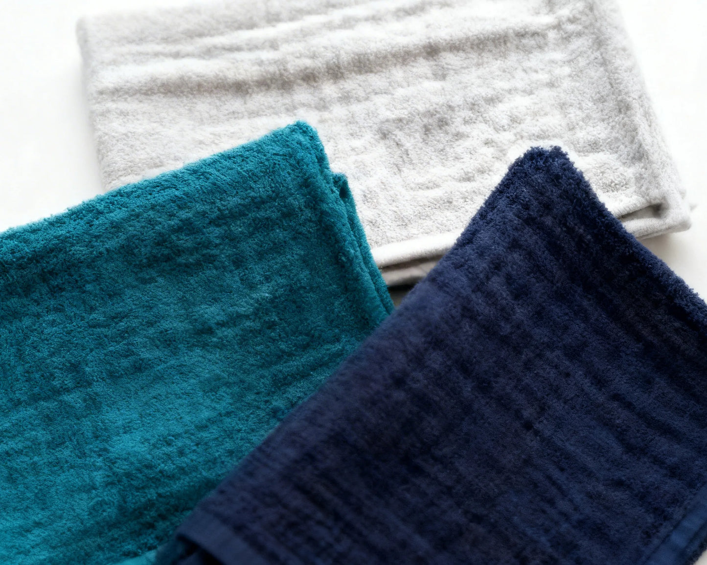 Set of folded blue, white, and gray hanky on a light surface with a coffee cup and plant.