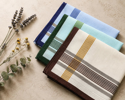 Set of folded cotton hanky with different patterns on a beige surface with dried plants.