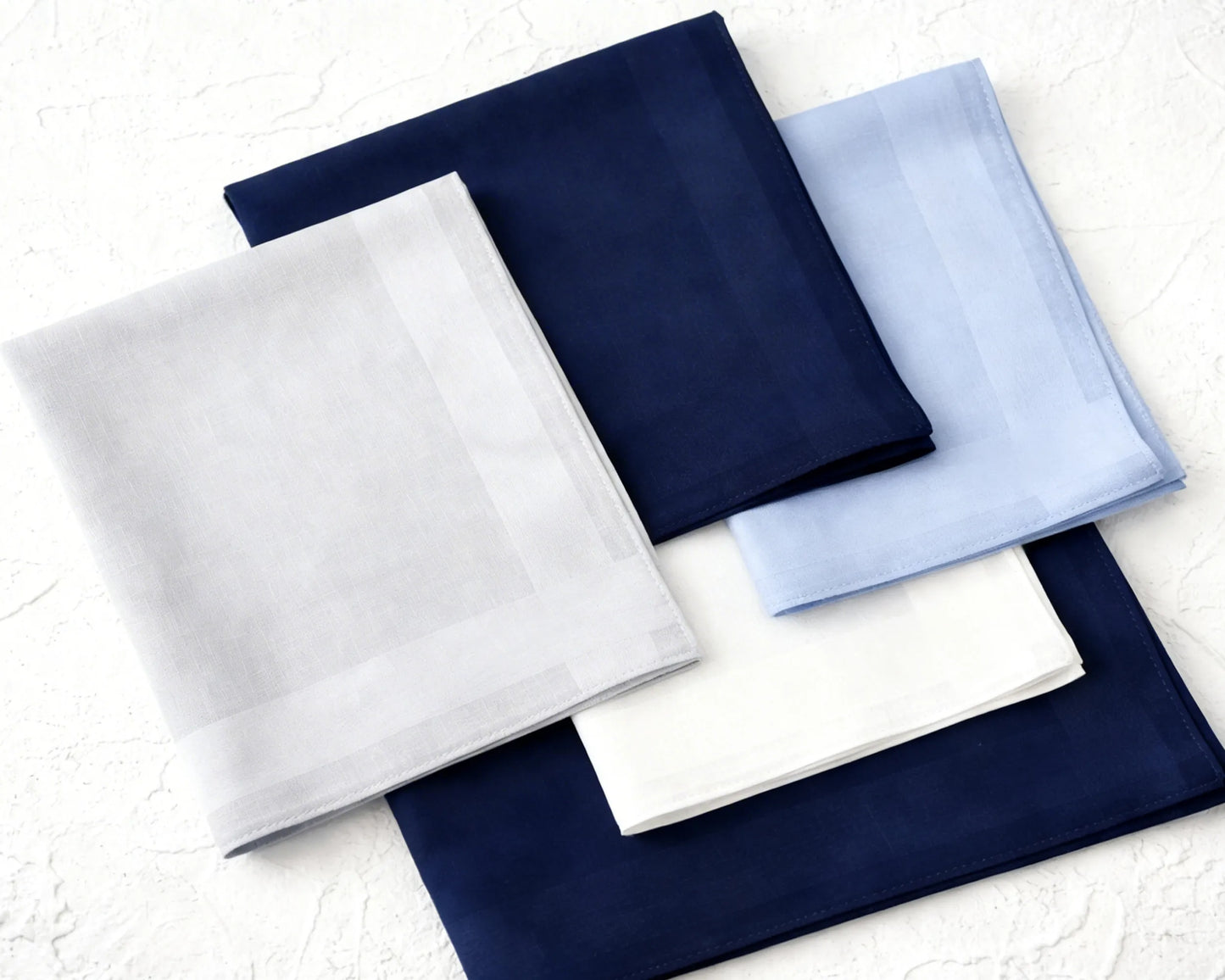 Set of folded fabric hanky in white, navy, and light blue on a textured surface.