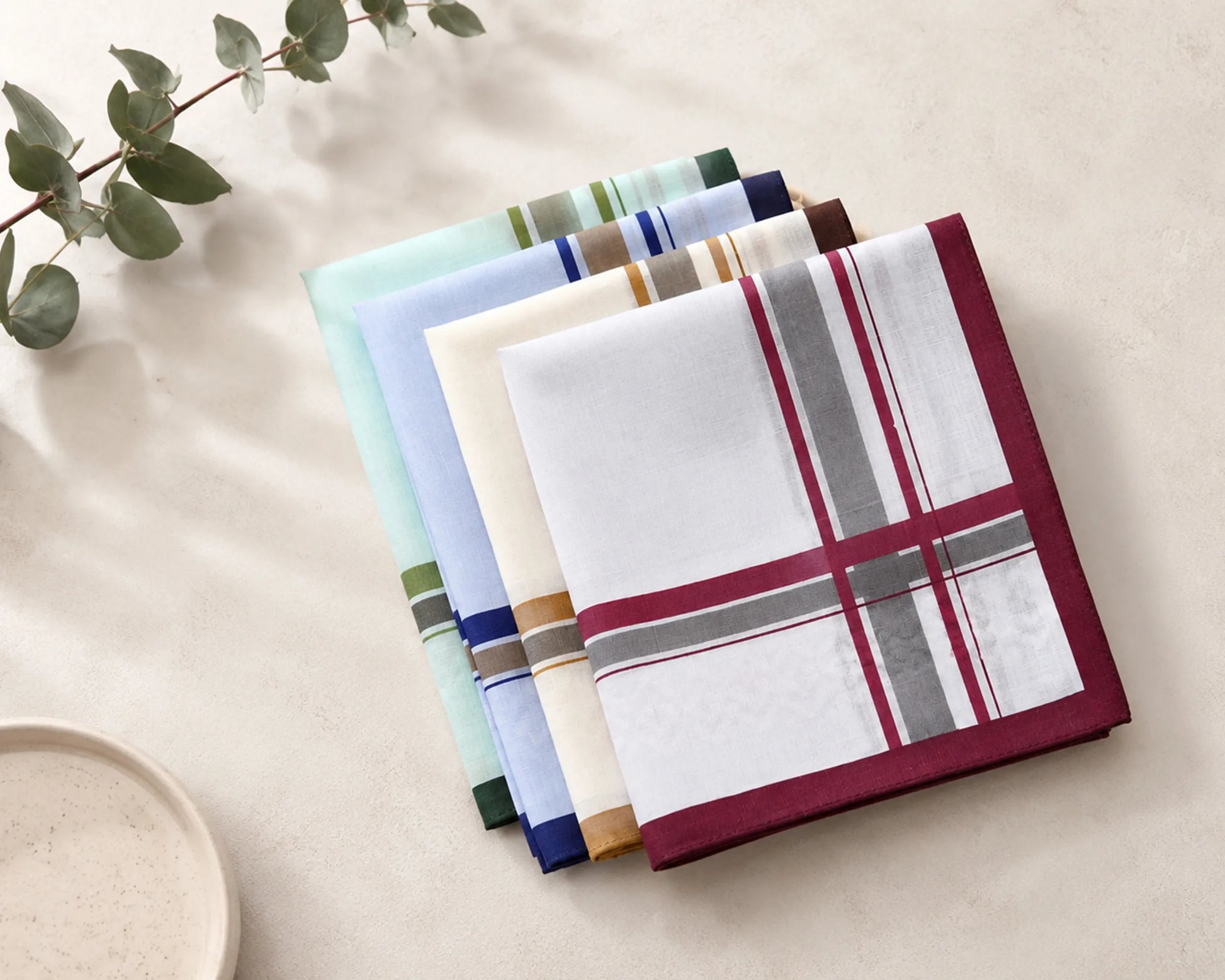 Set of folded plaid hanky on a neutral background with a branch of leaves.
