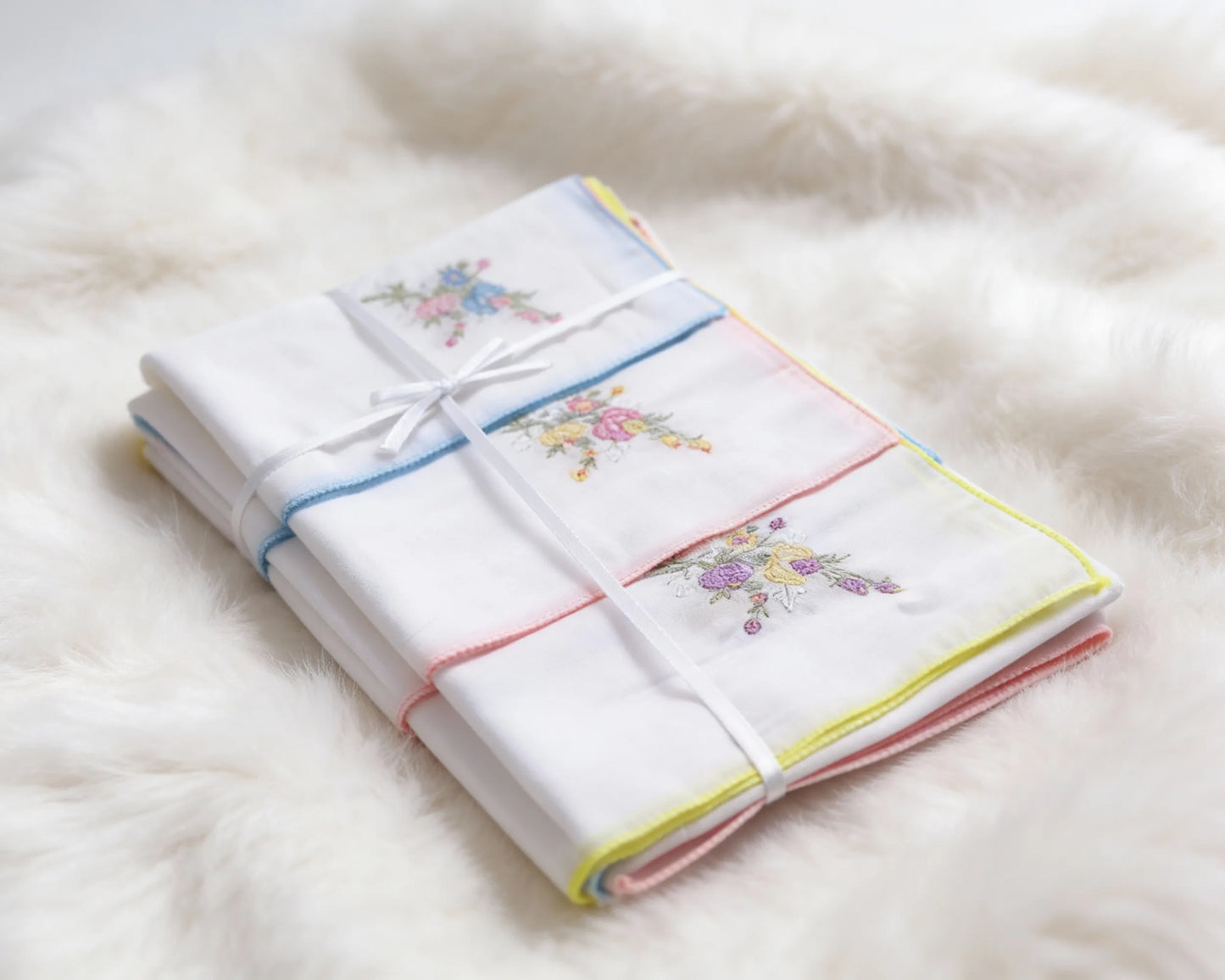Set of folded white towels with colorful embroidery on a fluffy white surface
