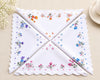 Set of four embroidered handkerchiefs with floral patterns on a beige surface.