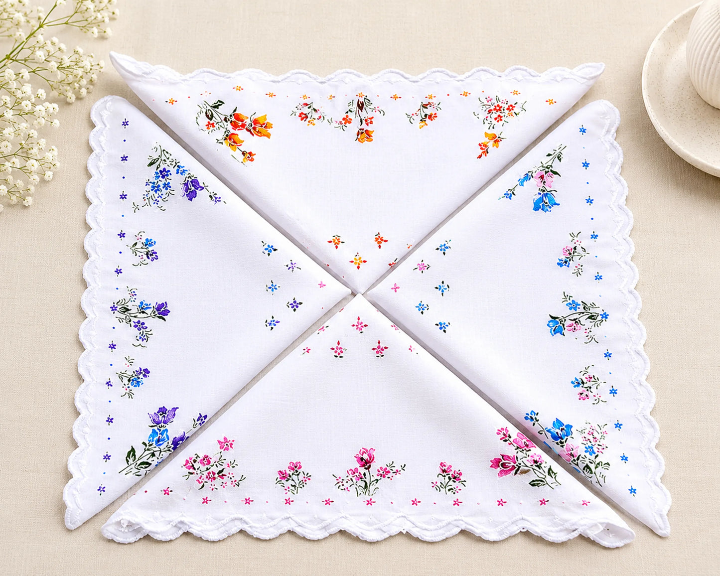 Set of four embroidered handkerchiefs with floral patterns on a beige surface.
