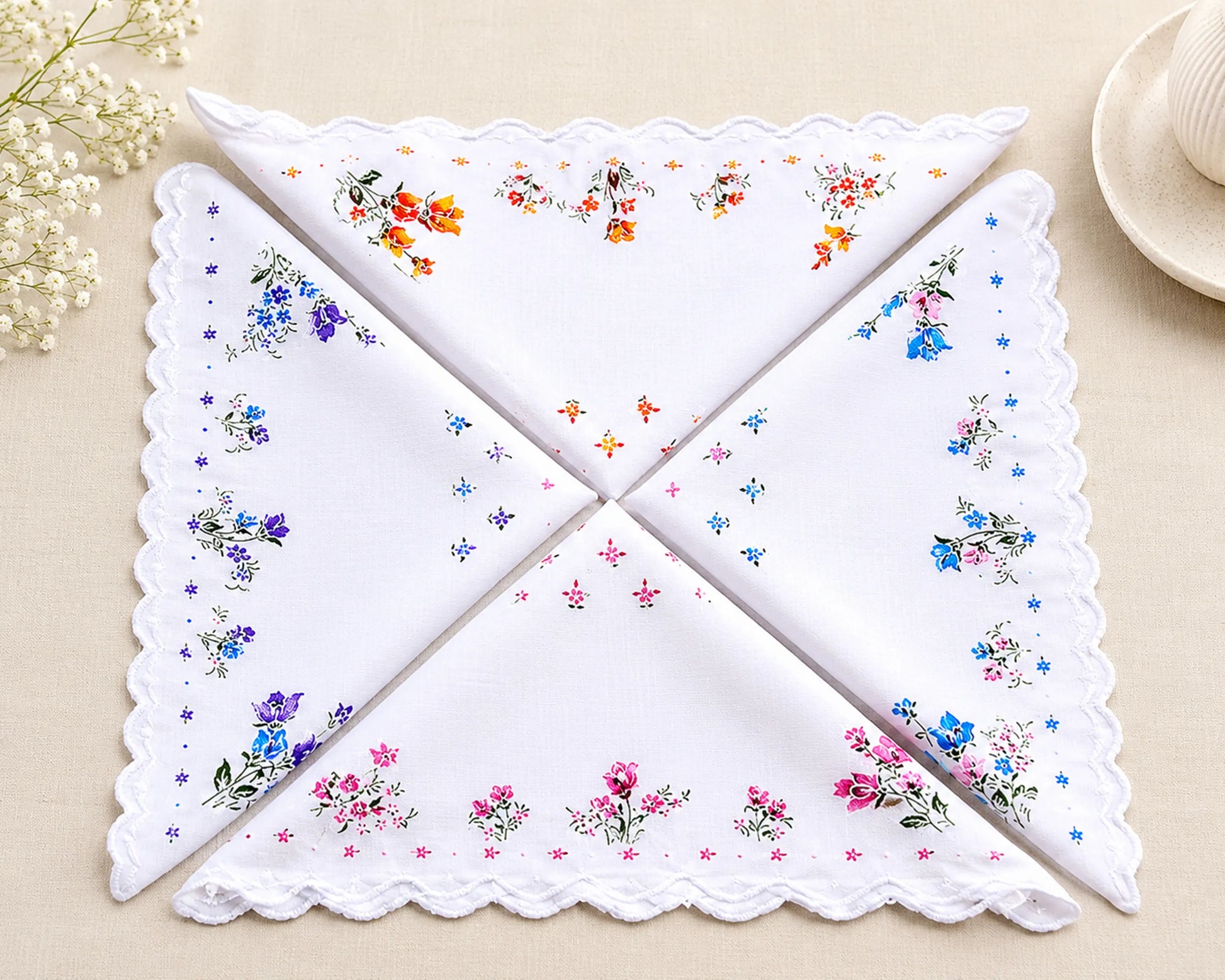 Set of four embroidered handkerchiefs with floral patterns on a beige surface.