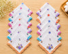 Set of embroidered handkerchiefs on a wooden surface with flowers in the background