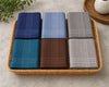 Set of six folded hanky in blue, gray, green, red, and brown on a marble surface.