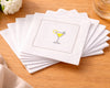 Set of white cocktail napkins with a martini glass design on a wooden surface.