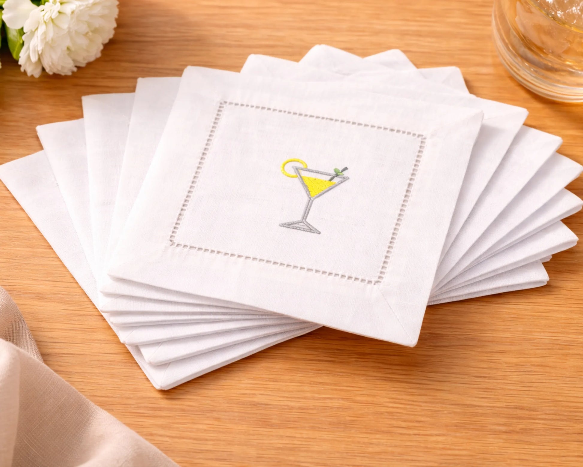 Set of white cocktail napkins with a martini glass design on a wooden surface.