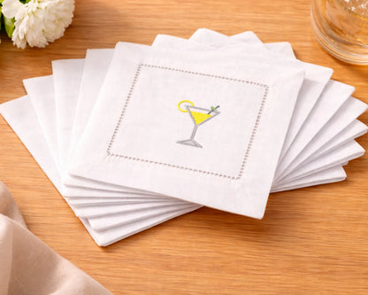 Set of white cocktail napkins with a martini glass design on a wooden surface.