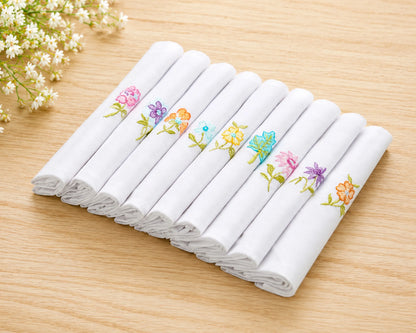 Set of white handkerchiefs with colorful floral embroidery on a wooden surface.
