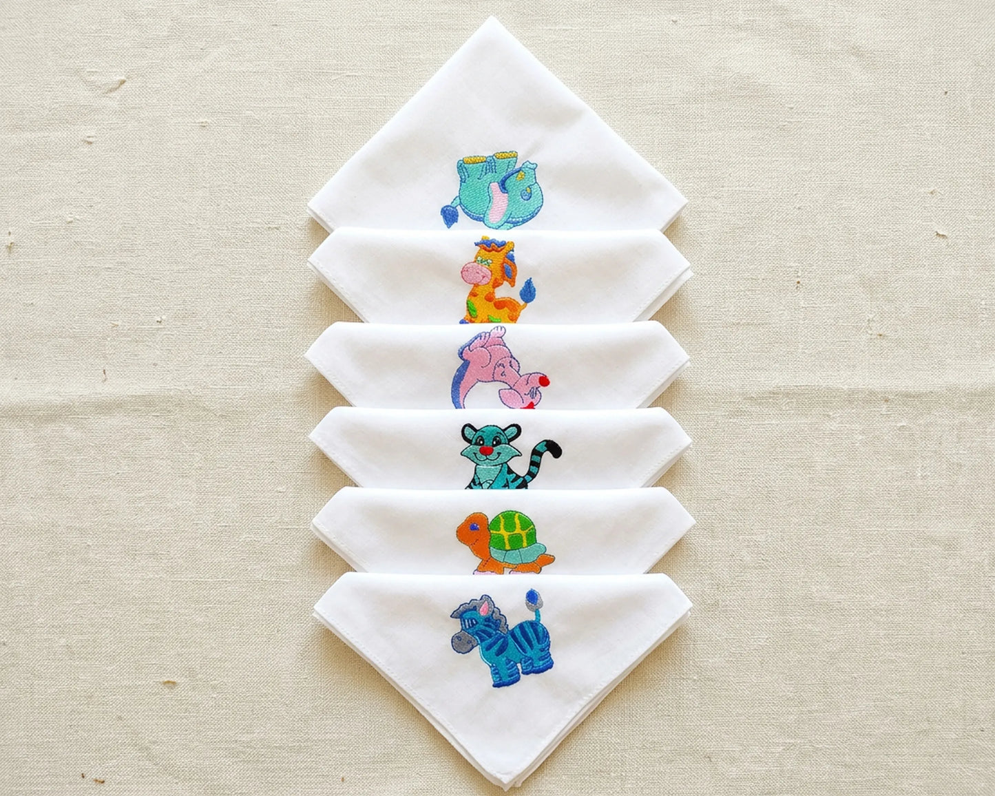 Set of white hanky with embroidered animal designs on a beige fabric background