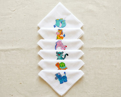 Set of white hanky with embroidered animal designs on a beige fabric background
