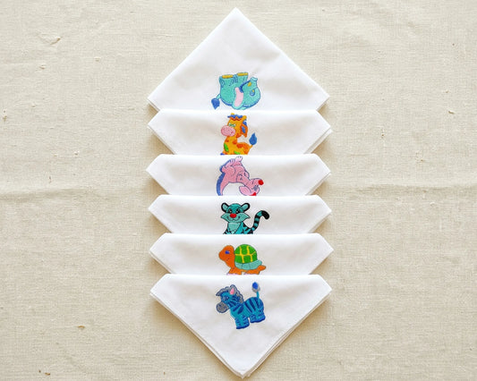 Set of white hanky with embroidered animal designs on a beige fabric background