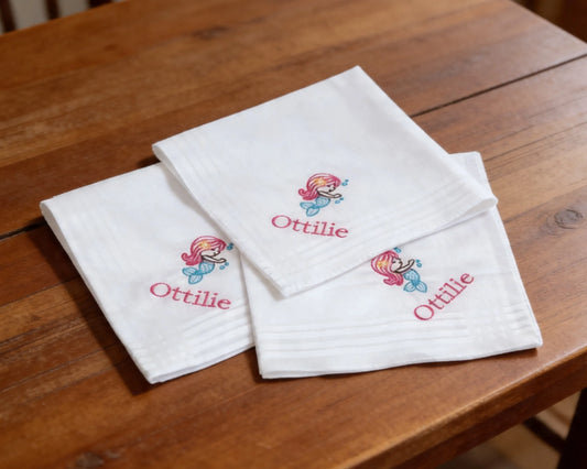 Set of white hanky with embroidered designs and 'Ottilie' text on a wooden surface
