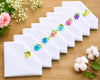 Set of white handkerchiefs with colorful floral embroidery on a wooden surface with flowers and cotton.