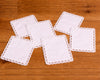 Set of white square coasters with lace edges on a wooden surface