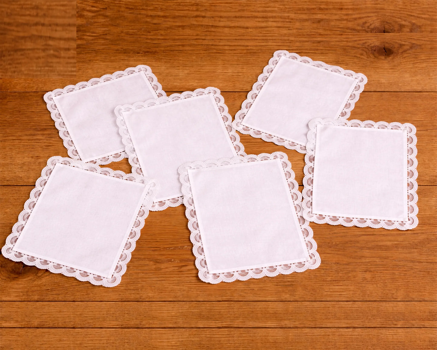 Set of white square coasters with lace edges on a wooden surface