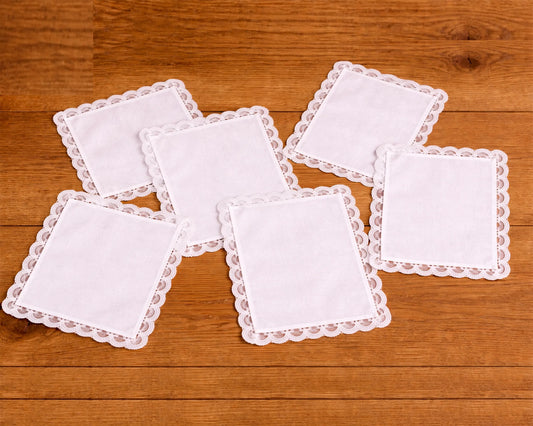 Set of white square coasters with lace edges on a wooden surface