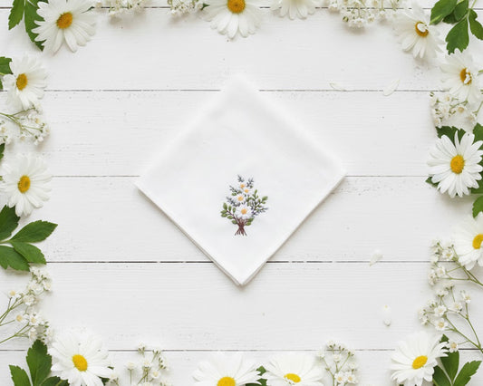 Centered embroidery of white daisies and green leaves on a white cotton handkerchief framed by real flowers