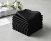 Stack of black folded handkerchief  on a light gray surface with white flowers in the background.