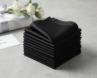 Stack of black folded handkerchief  on a light gray surface with white flowers in the background.