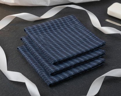 Stack of blue checkered hanky on a dark surface with white ribbons.