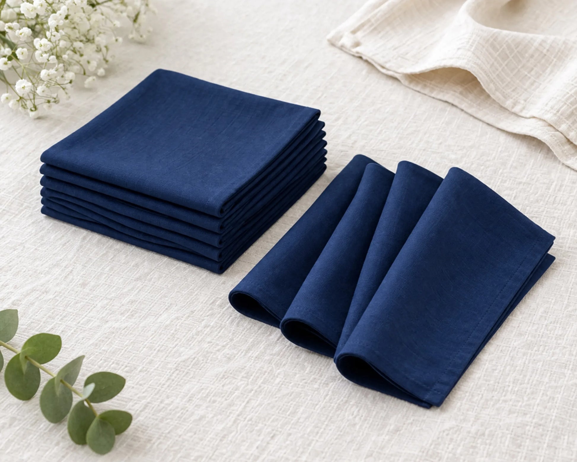 Stack of blue handkerchief on a white surface with a beige towel and white flowers in the background.