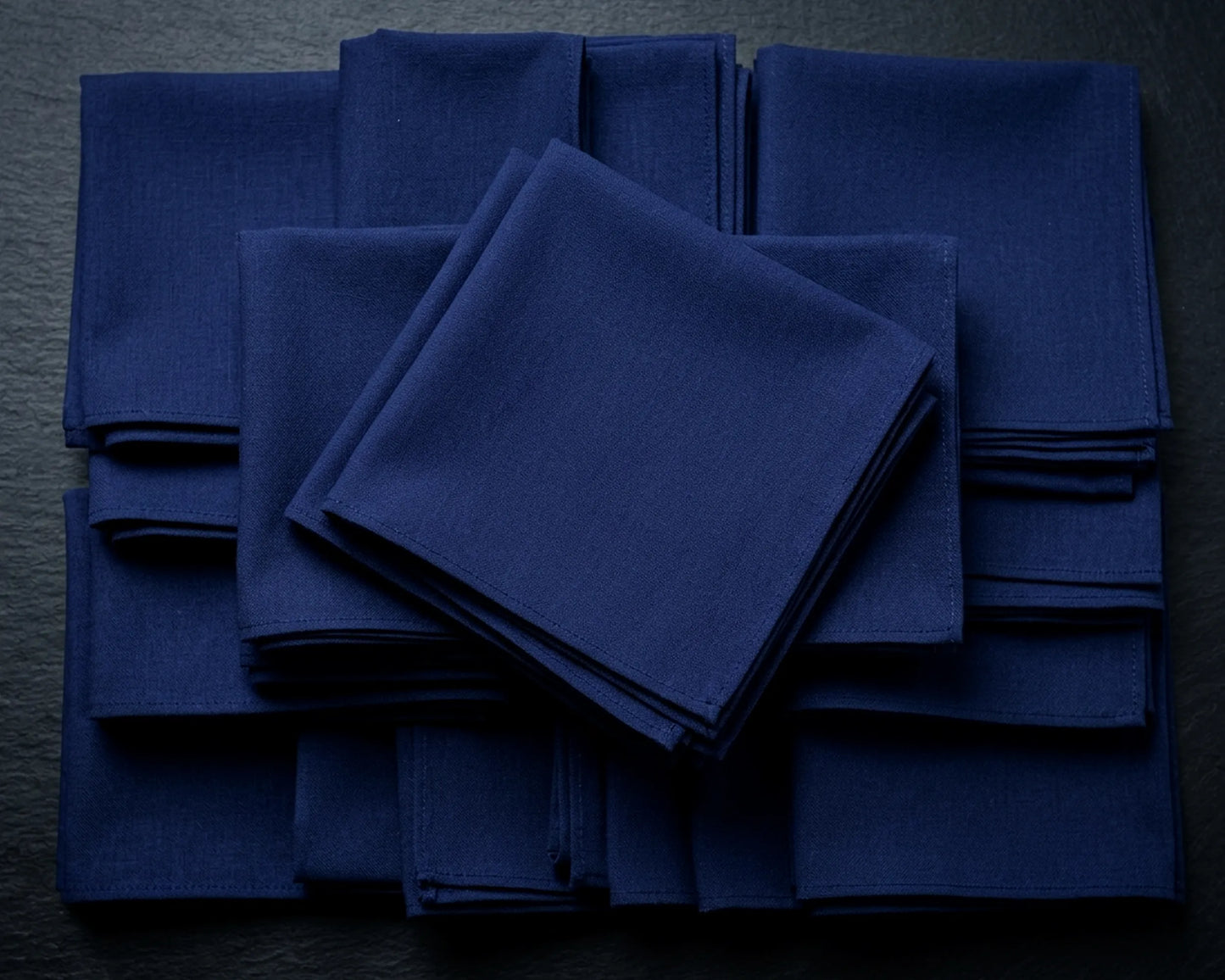 Stack of blue napkins on a beige surface with green leaves.