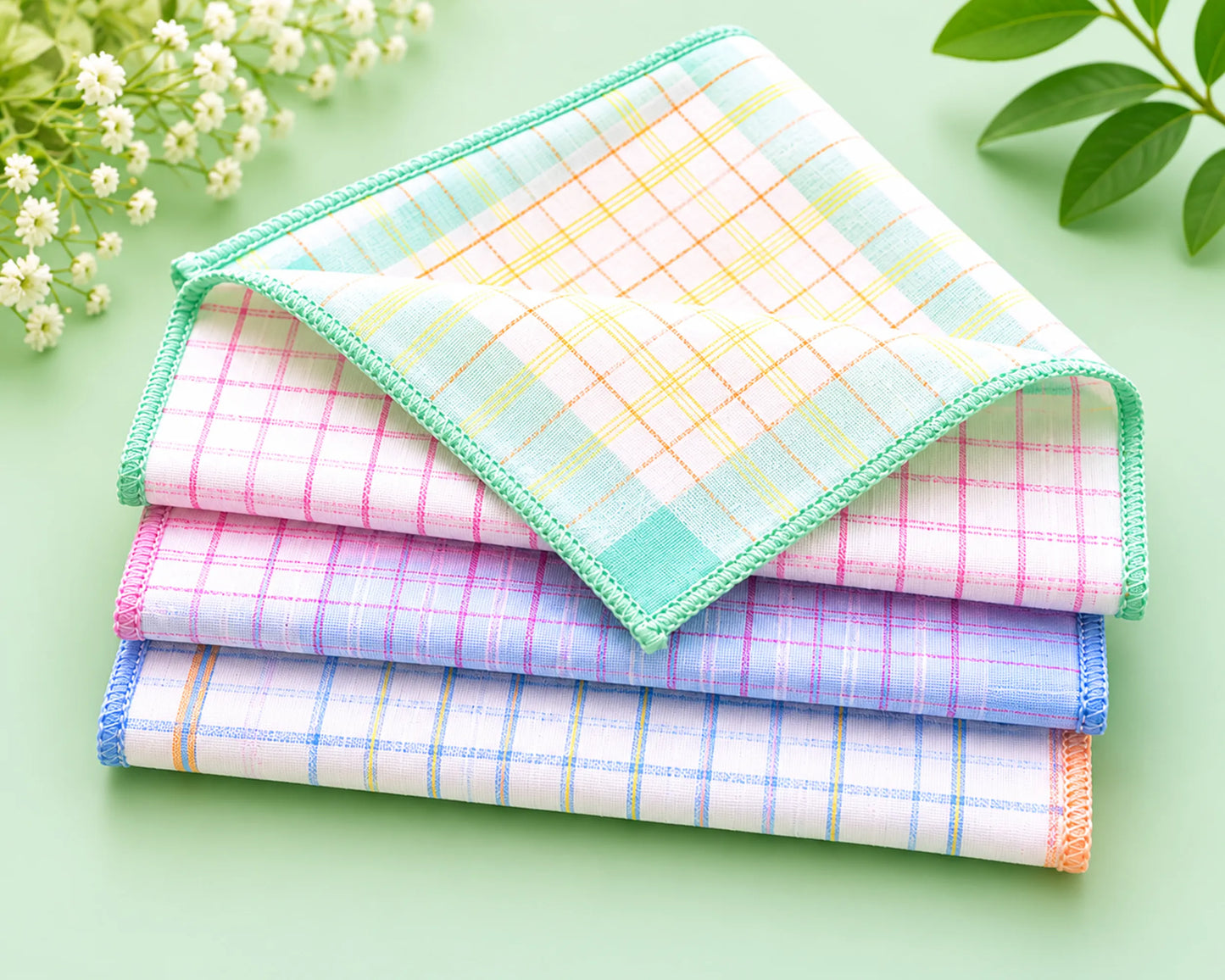 Stack of colorful checkered handkerchiefs on a light green background with flowers and leaves.