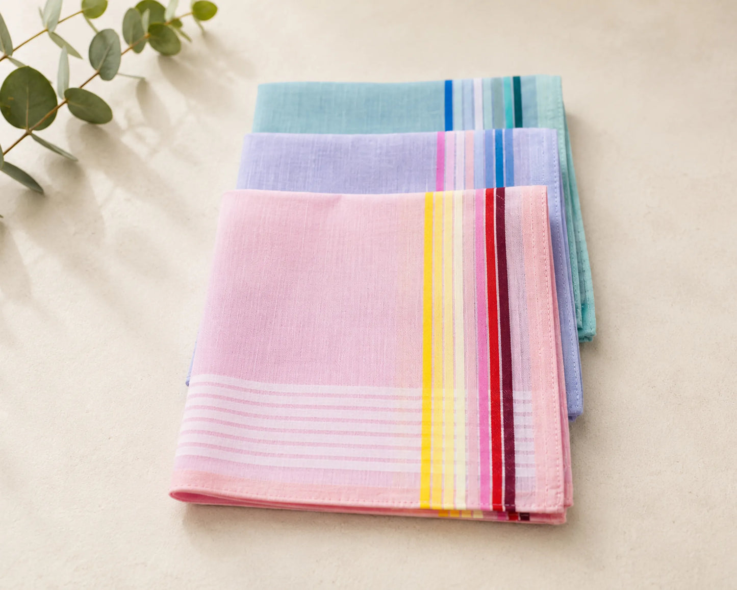 Stack of colorful striped hanky on a light surface with greenery.