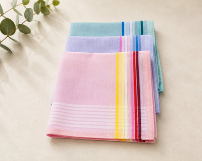 Stack of colorful striped hanky on a light surface with greenery.