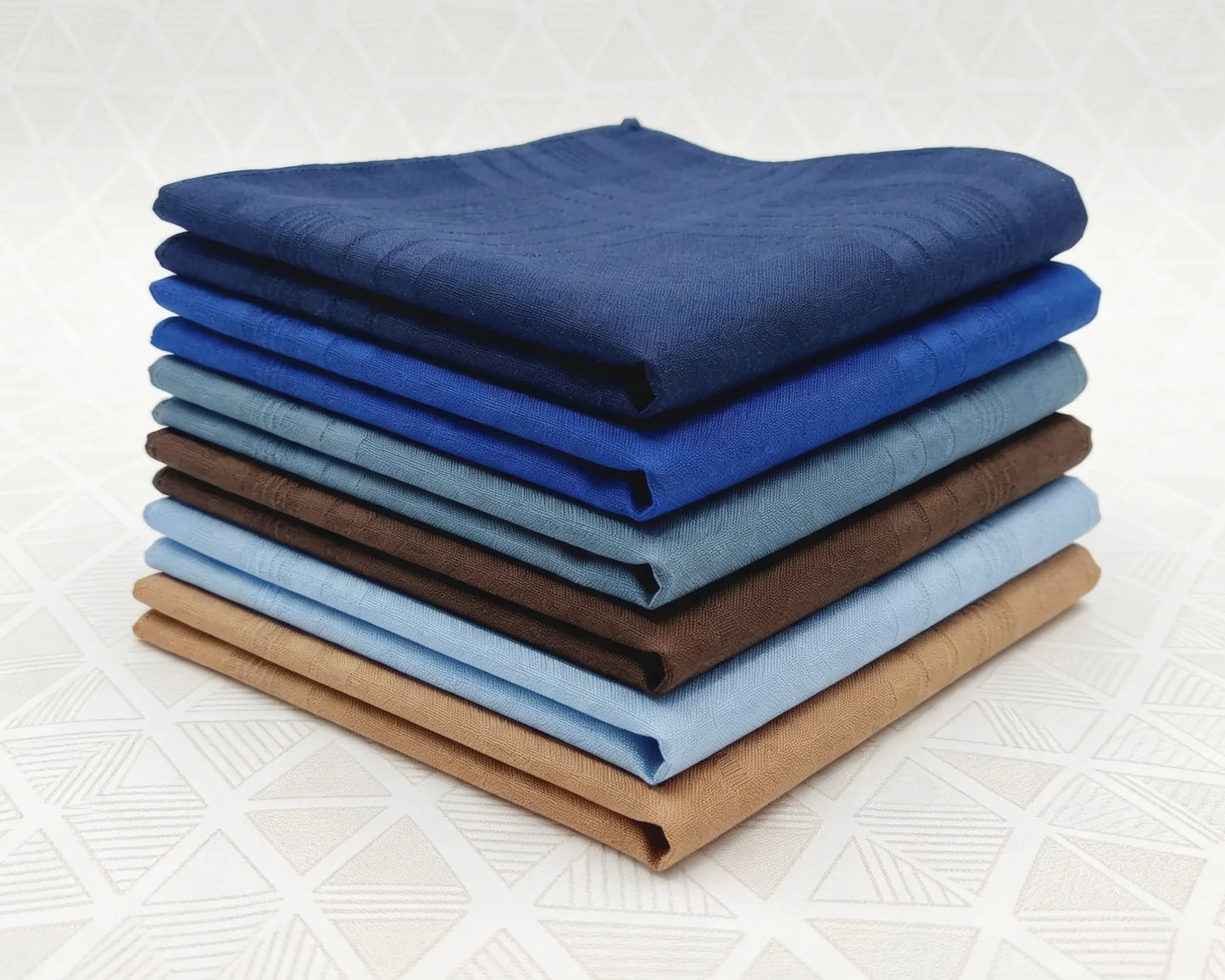Stack of folded cotton hanky in various blue and brown shades on a white background