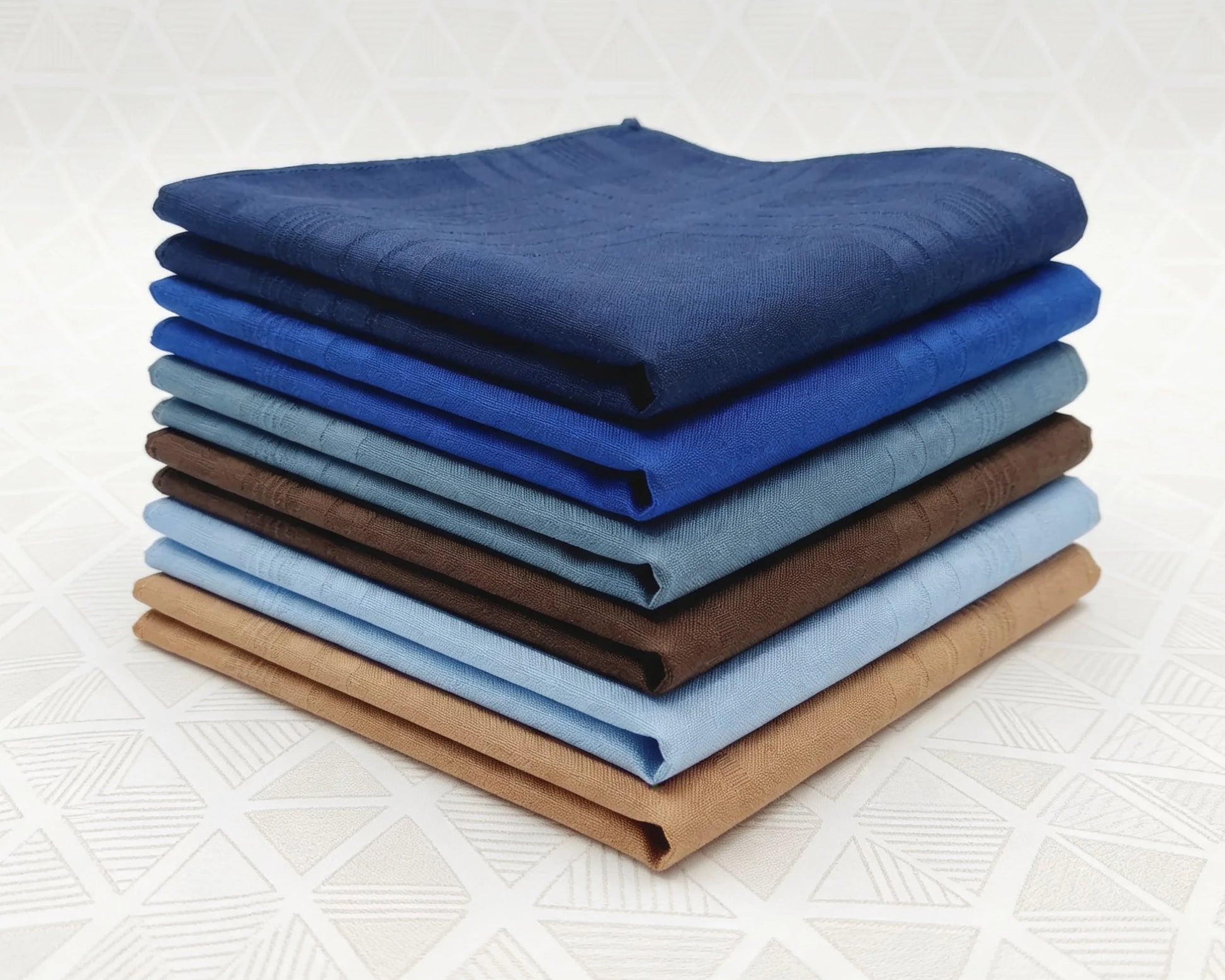 Stack of folded cotton hanky in various blue and brown shades on a white background