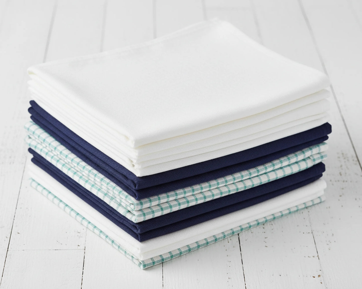 Stack of folded hanky in white, navy, and green checkered patterns on a light wooden surface.